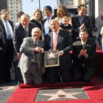 Man in a suit holding a Hollywood star plaque while posing with other people in the Hollywood Walk of Fame